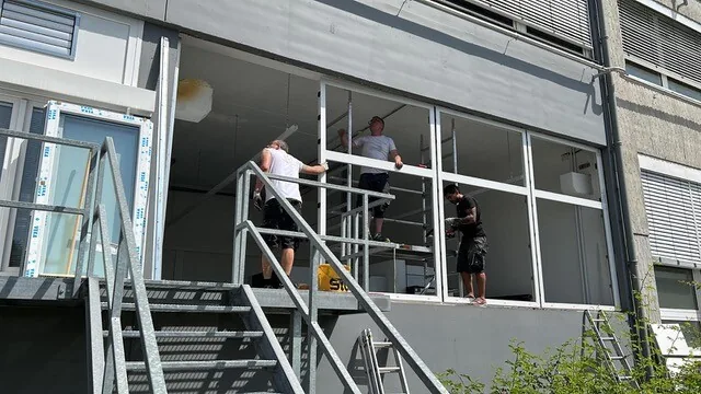 Monteure setzen große Fensterelemente an einem Balkon ein
